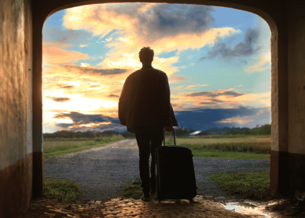 Man rolling luggage case walks into picturesque sunset